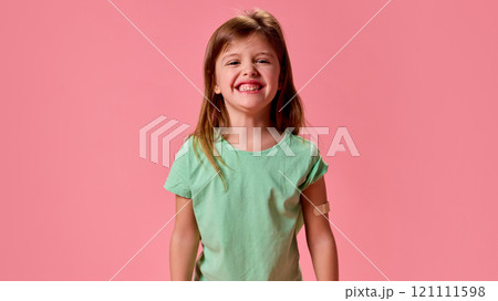 Happy, cheerful smiling and healthy little schoolgirl with patch on hand after vaccination against pastel pink background. 121111598
