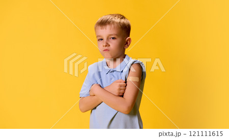 Unhappy little kid, boy crossed hands with patch after vaccination on chest against yellow background. Unhappy little kid, boy crossed hands with patch after vaccination on chest against yellow background. 121111615