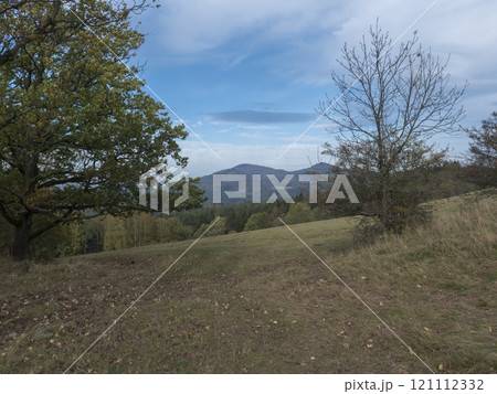Meadow with autumn colorful forest, trees and hills, moody sky. Landscape in Luzicke hory Lusatian Mountains, Czech Republic. 121112332