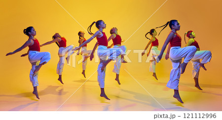 Dynamic image of teen girls in same outfits in motion, performing hip hop, dancing against yellow background in neon light 121112996
