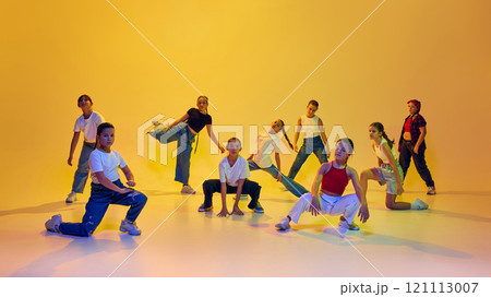 Dance club. Young girls, teenagers wearing stylish casual clothes, training, dancing hip hop against yellow background in neon light. 121113007