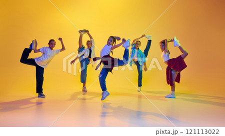 Youth culture. Group of teen girls, friends wearing casual clothes, dancing hip hop, learning new moves against yellow background in neon light 121113022
