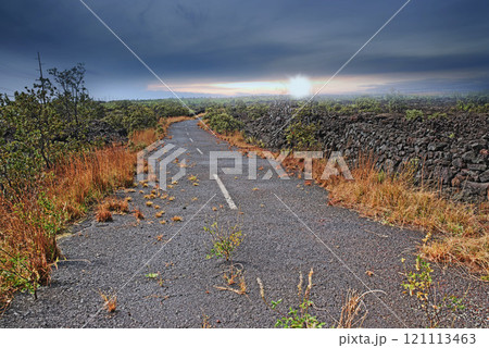Empty road through a field with burnt grass and cloudy sky with copy space. A curved countryside road or open asphalt roadway between dry land near Mauna Kea volcanic mountainside, Hawaii, Big Island Empty road through a field with burnt grass and cloudy sky with copy space. A curved countryside road or open asphalt roadway between dry land near Mauna Kea volcanic mountainside, Hawaii, Big Island 121113463