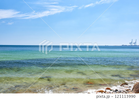 Landscape view of a blue ocean with clear skies on the horizon on a warm summer day. Little waves crash on a quiet calm rocky shore in the mediterranean sea. Panoramic coastline location for tourist Landscape view of a blue ocean with clear skies on the horizon on a warm summer day. Little waves crash on a quiet calm rocky shore in the mediterranean sea. Panoramic coastline location for tourist 121113990