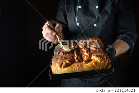 A skilled chef applies a delicate glaze to a freshly baked loaf of bread while holding it in a dark kitchen. The aroma of warm yeast fills the air as the crust shines 121114321