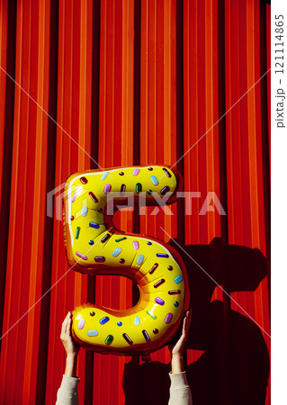 man holds the number 5 against a red wall man holds the number 5 against a red wall 121114865