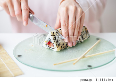 The process of making sushi, the girl makes sushi with different flavors - fresh salmon, caviar, avocado, cucumber, ginger, rice. Cut the roll into pieces. Close-up. The process of making sushi, the girl makes sushi with different flavors - fresh salmon, caviar, avocado, cucumber, ginger, rice. Cut the roll into pieces. Close-up. 121115164