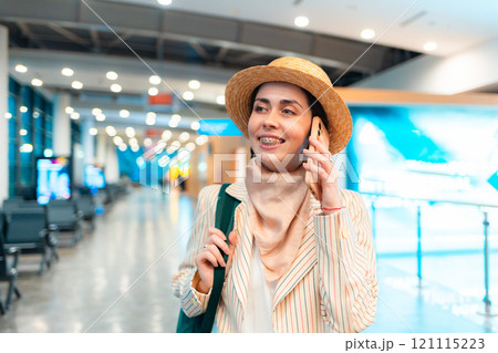 Portrait of young Caucasian woman in a hat and jacket smiling and walks through the airport and talking to the smartphone. Concept of boarding at terminal before flight 121115223
