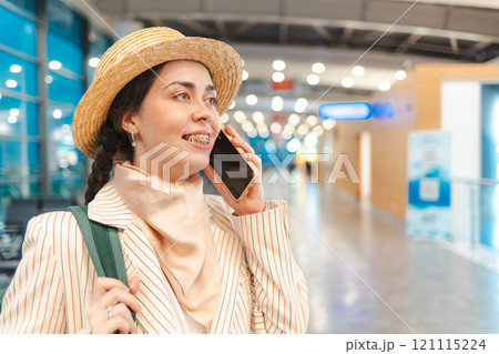 Portrait of young Caucasian woman in a hat and jacket smiling and talking to the smartphone in airport. Copy space. Concept of boarding at terminal before flight Portrait of young Caucasian woman in a hat and jacket smiling and talking to the smartphone in airport. Copy space. Concept of boarding at terminal before flight 121115224