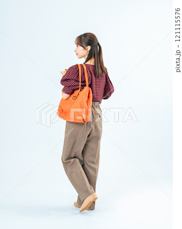 スマホを持って歩くカジュアルウェアの女性の後ろ姿の全身写真 121115576