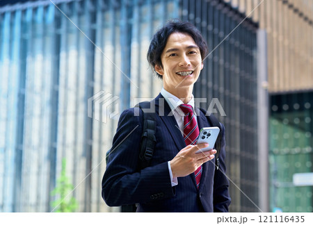 スマホを操作するリュックを担いだスーツ姿のビジネスマン 121116435