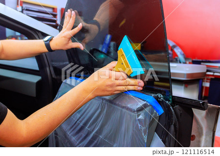 Technician applies window tint to car door while ensuring smooth finish in vibrant auto repair environment. 121116514