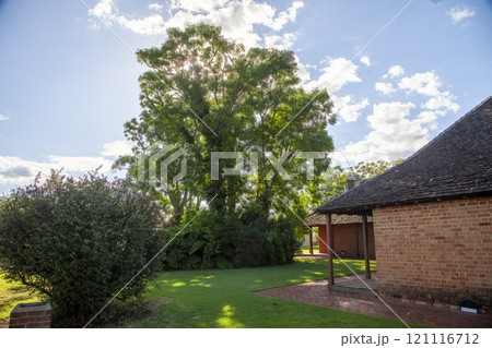 Charming heritage building surrounded by lush trees and greenery under a sunny sky 121116712