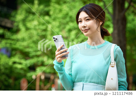ショッピングしながらスマホを操作するオシャレな若い女性 ショッピングしながらスマホを操作するオシャレな若い女性 121117486