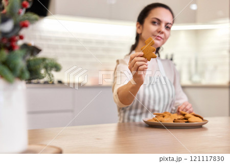 Beautiful woman holding plate of delicious gingerbread cookies in the kitchen, focus on cookies. Christmas time 121117830