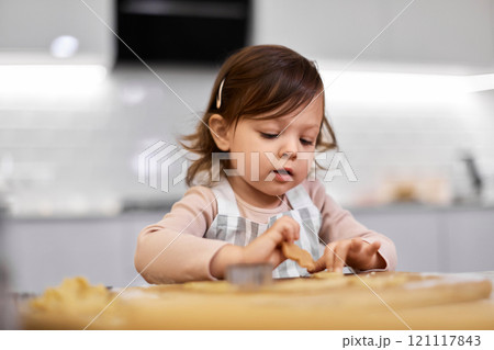 cute little child girl cutting gingerbread cookies with a cookie cutter in kitchen. festive gingerbread cookies 121117843
