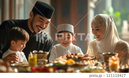 Joyful family scene showing Muslim family enjoying meal together. Father, mother, son, and daughter dressed in traditional attire. 121118427