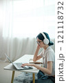 A woman wearing headphones and glasses is typing on a laptop 121118732