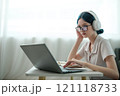 A woman wearing headphones and glasses is typing on a laptop 121118733