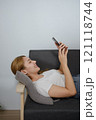 A woman is laying on a couch and looking at her phone 121118744