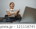A woman is sitting on a couch with a laptop open in front of her 121118745
