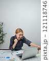 A woman is sitting at a desk with a laptop open 121118746