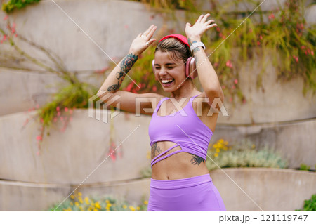 A Joyful Woman Dancing Happily in Stylish Workout Gear While Enthusiastically Wearing Headphones 121119747