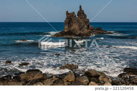 A dramatic coastal scene featuring a rugged rock formation surrounded by ocean waves 121120458