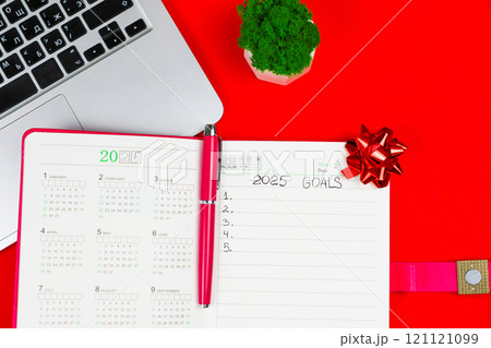 Close-up of a pink notebook diary in which it is written: Goals for 2025, inside it is a calendar for 2025 and there is a pink pen and in the upper right corner there is a festive New Year's bow on a Close-up of a pink notebook diary in which it is written: Goals for 2025, inside it is a calendar for 2025 and there is a pink pen and in the upper right corner there is a festive New Year's bow on a 121121099