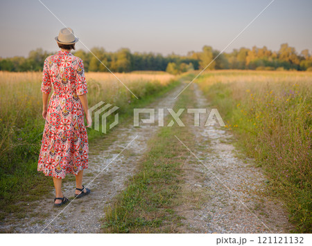 Young woman walking through picturesque European field in late summer. Golden sunlight, lush greenery, and serene rural atmosphere create peaceful countryside scene. Young woman walking through picturesque European field in late summer. Golden sunlight, lush greenery, and serene rural atmosphere create peaceful countryside scene. 121121132