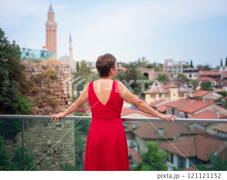 Woman in red dress walking narrow streets of old town Antalya during warm summer evening. Historic atmosphere and Mediterranean charm creates peaceful travel experience. view on Kalechi 121121152
