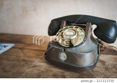 A vintage rotary dial telephone with a worn metallic finish sits on a rustic wooden surface, set against a simple textured wall in a Marrakech themed hotel. 121121530