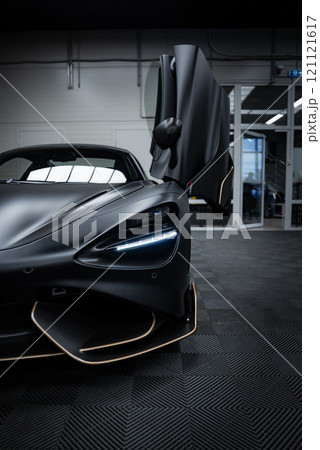 The McLaren 720S is displayed indoors, featuring a matte black finish with gold trim. Its open butterfly door and industrial setting are highlighted. The McLaren 720S is displayed indoors, featuring a matte black finish with gold trim. Its open butterfly door and industrial setting are highlighted. 121121617