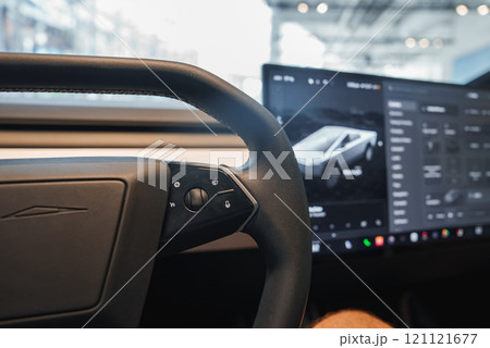 The image captures a Tesla vehicle's interior, highlighting the steering wheel and central touchscreen with a Cybertruck interface, in a well lit showroom. 121121677