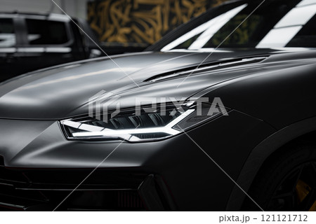 The image features the front section of a Lamborghini Urus Performante, focusing on its angular LED headlights and smooth hood lines. A hint of abstract wall art is visible in the background The image features the front section of a Lamborghini Urus Performante, focusing on its angular LED headlights and smooth hood lines. A hint of abstract wall art is visible in the background 121121712