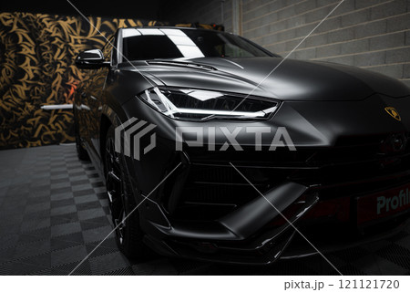 The image features a matte black Lamborghini Urus Performante indoors, with a gold and black patterned wall and checkered floor enhancing its sporty design. 121121720