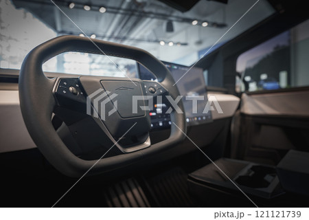 Interior of a futuristic vehicle featuring a unique steering wheel and large touchscreen display, set in a showroom with modern architectural elements. 121121739