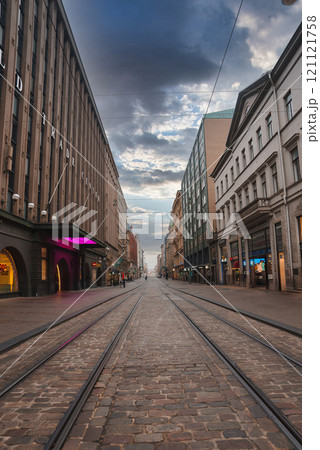 View of a cobblestone street in Helsinki, Finland, featuring tram tracks, historic buildings, and a partly cloudy sky, creating a serene urban scene. 121121758