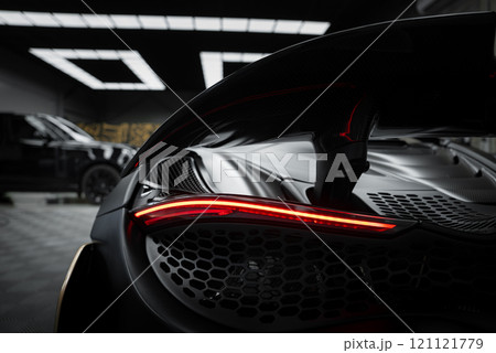 The image captures the McLaren 720S rear, showcasing its aerodynamic design, carbon fiber details, and distinctive rear light in a modern indoor showroom. 121121779
