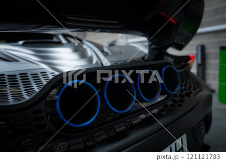 The image shows the rear section of a McLaren 720S, featuring quad exhaust pipes with blue accents. The setting includes a brick wall and industrial elements. The image shows the rear section of a McLaren 720S, featuring quad exhaust pipes with blue accents. The setting includes a brick wall and industrial elements. 121121783