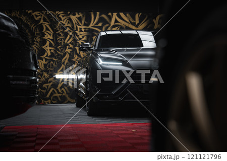 A close up view of a Lamborghini Urus Performante indoors, with gold and black patterns in the backdrop. Red and black checkered flooring is visible. 121121796