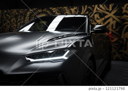 A close up view of a Lamborghini Urus Performante indoors, featuring its angular design and LED headlights against a gold and black patterned wall. 121121798