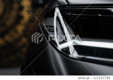 Detailed view of a Lamborghini Urus Performante headlight, showcasing intricate design and branding. Blurred background with a hint of pattern. 121121799