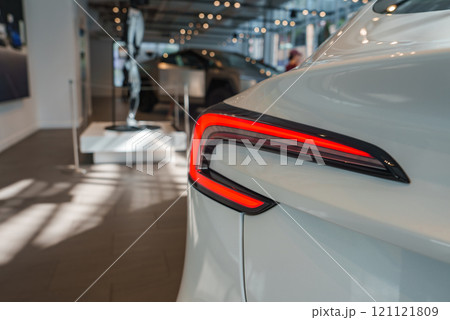 A sleek car with unique red taillights is displayed in a bright showroom. The polished floor and contemporary decor enhance the vehicle's glossy finish. A sleek car with unique red taillights is displayed in a bright showroom. The polished floor and contemporary decor enhance the vehicle's glossy finish. 121121809