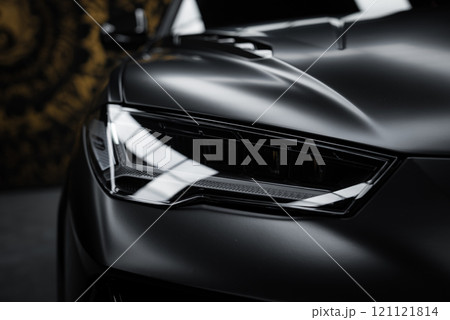 The image captures the angular headlight of a Lamborghini Urus Performante, highlighting its matte black finish and sharp design against a patterned background. The image captures the angular headlight of a Lamborghini Urus Performante, highlighting its matte black finish and sharp design against a patterned background. 121121814
