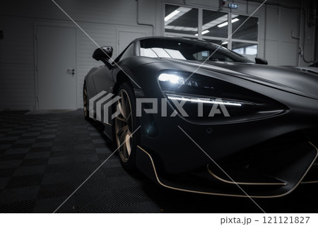 The image shows a McLaren 720S parked indoors on a checkered floor. The sleek design, LED headlights, and matte finish are highlighted by the lighting. 121121827