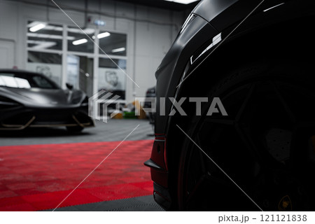 A close up view of a Lamborghini Urus Performante with a sleek black exterior. The McLaren 720S is partially visible in a well lit garage with a checkered floor. 121121838