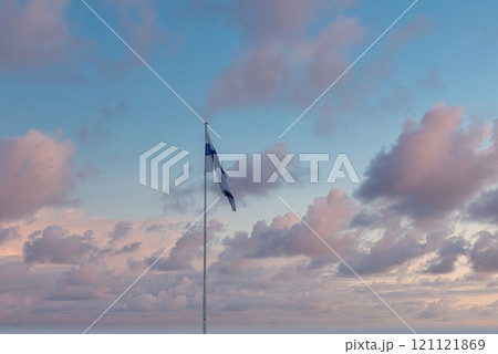 A Finnish flag waves prominently against a serene sky with pastel clouds, showcasing blue and white colors. The scene suggests dawn or dusk in Helsinki. A Finnish flag waves prominently against a serene sky with pastel clouds, showcasing blue and white colors. The scene suggests dawn or dusk in Helsinki. 121121869
