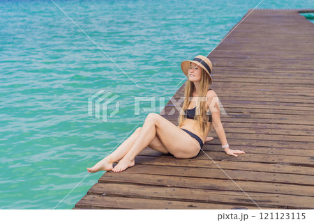 Woman in swimsuit sitting on a pier at Lake Bacalar. Quintana Roo, Mexico travel, summer relaxation, and waterfront serenity concept 121123115