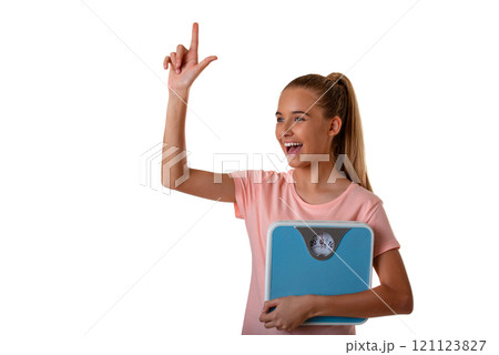Portrait of young smiling girl in pink t-shirt holding weighing scale and pointing her finger in eureka sign, having great innovative idea. Isolated 121123827